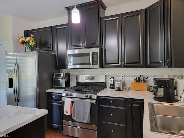 kitchen featuring light stone counters, hanging light fixtures, stainless steel appliances, and backsplash