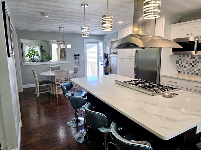 kitchen with appliances with stainless steel finishes, island exhaust hood, hanging light fixtures, white cabinetry, and dark wood-type flooring