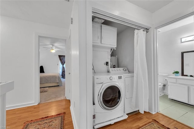 clothes washing area featuring light hardwood / wood-style flooring, water heater, washing machine and clothes dryer, ceiling fan, and cabinets