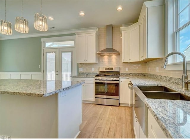 kitchen with wall chimney range hood, light wood-type flooring, white cabinetry, pendant lighting, and stainless steel gas range oven