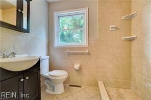 bathroom with toilet, vanity, tile patterned floors, and tile walls