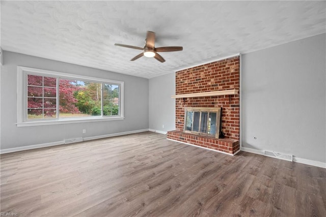 unfurnished living room with a brick fireplace, ceiling fan, a textured ceiling, and hardwood / wood-style flooring