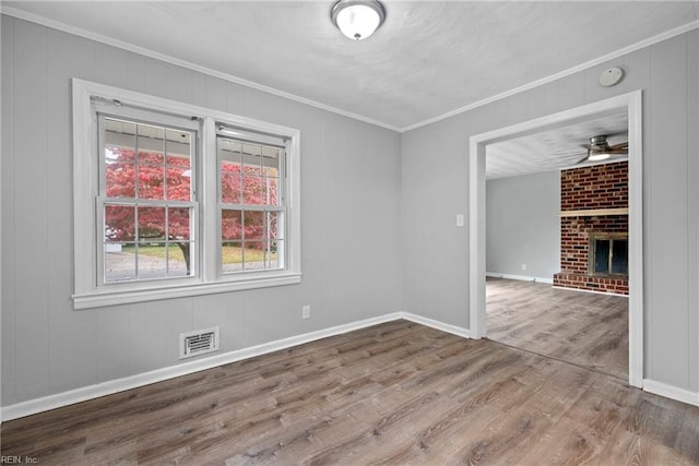 spare room with ceiling fan, wood-type flooring, crown molding, and a brick fireplace