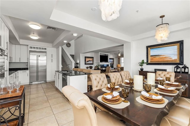 dining room with a raised ceiling, sink, ceiling fan with notable chandelier, and light tile patterned floors