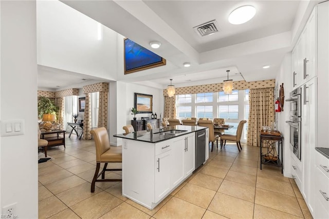 kitchen with dishwasher, a kitchen bar, hanging light fixtures, white cabinetry, and light tile patterned floors