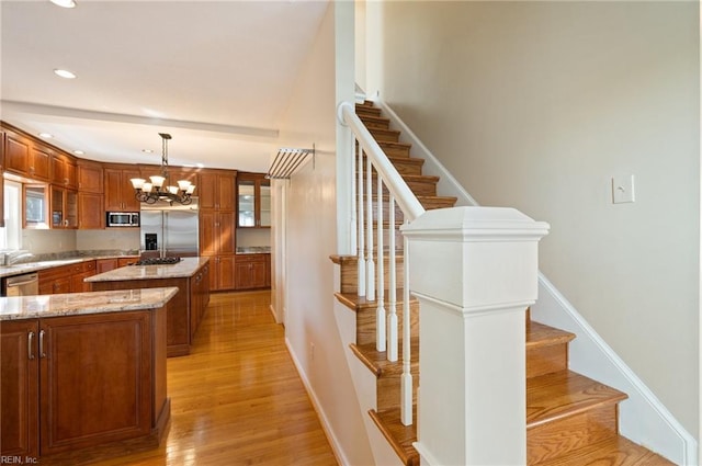 kitchen featuring light stone countertops, light wood-type flooring, a center island, hanging light fixtures, and stainless steel appliances