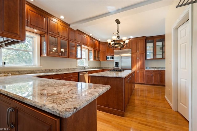 kitchen featuring light wood-type flooring, a center island, stainless steel appliances, a wealth of natural light, and decorative light fixtures