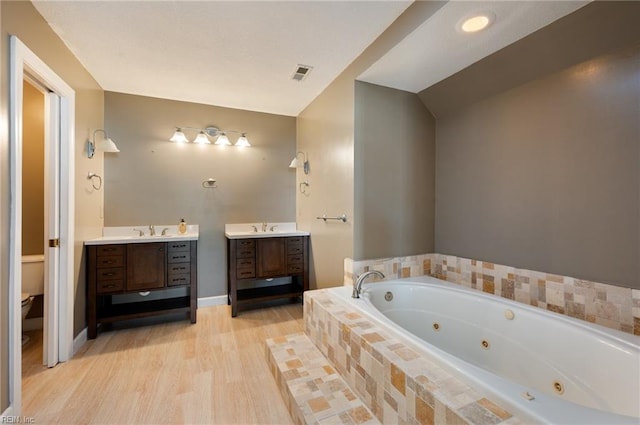 bathroom featuring vanity, toilet, tiled tub, and wood-type flooring