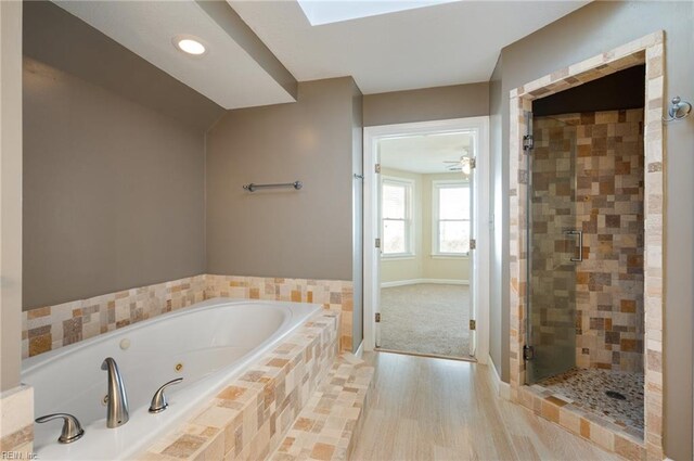 bathroom featuring ceiling fan, independent shower and bath, wood-type flooring, and vaulted ceiling with skylight