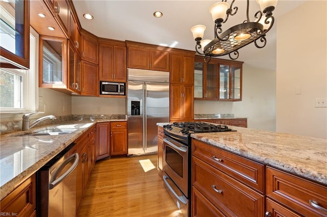 kitchen featuring sink, light wood-type flooring, decorative light fixtures, built in appliances, and light stone counters