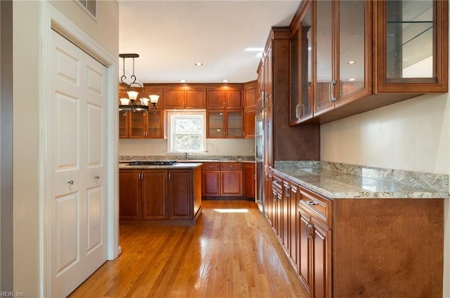 kitchen featuring light wood-type flooring, decorative light fixtures, gas cooktop, light stone counters, and an inviting chandelier