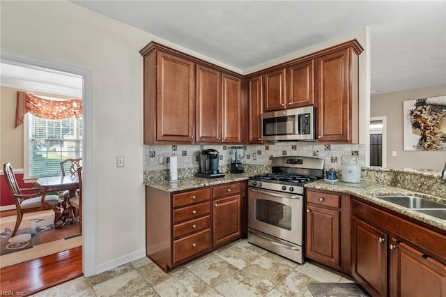 kitchen with sink, backsplash, stainless steel appliances, light stone counters, and a notable chandelier