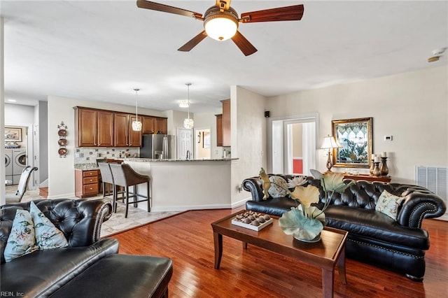 living room with ceiling fan, washer and clothes dryer, and dark hardwood / wood-style flooring