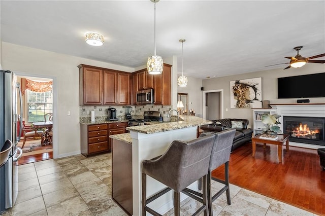 kitchen with kitchen peninsula, appliances with stainless steel finishes, light stone countertops, a kitchen bar, and decorative light fixtures