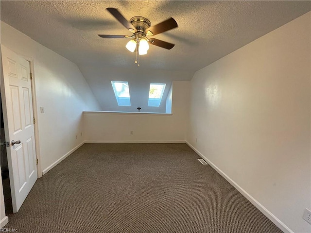 spare room with lofted ceiling with skylight, ceiling fan, a textured ceiling, and dark colored carpet