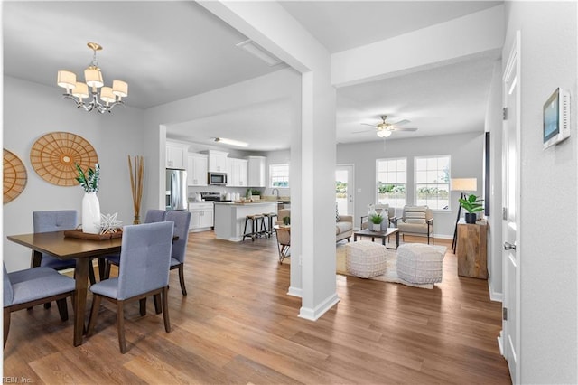 dining room with light hardwood / wood-style flooring and ceiling fan with notable chandelier