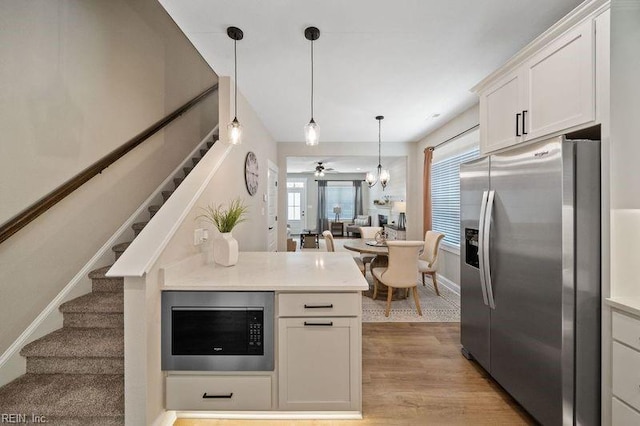 kitchen with kitchen peninsula, white cabinetry, light wood-type flooring, decorative light fixtures, and stainless steel appliances