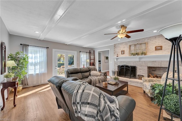 living room featuring ceiling fan, light wood-type flooring, a fireplace, french doors, and beam ceiling