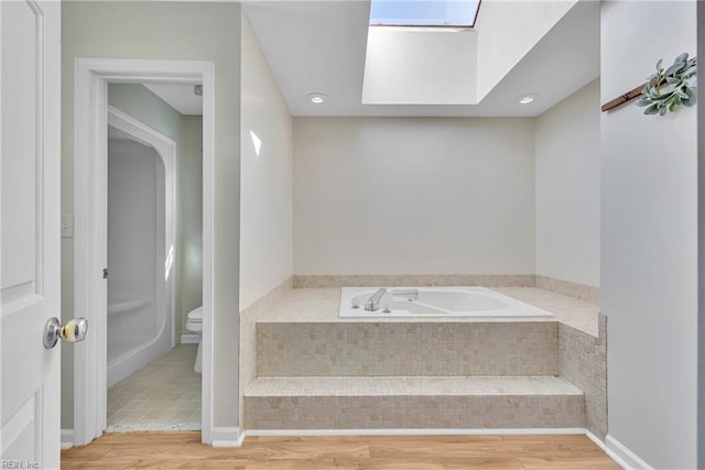 bathroom with tiled bath, hardwood / wood-style floors, toilet, and a skylight