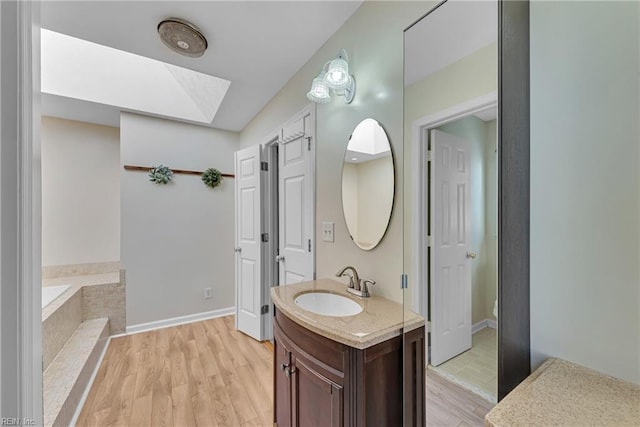 bathroom featuring tiled tub, vanity, a skylight, and hardwood / wood-style floors