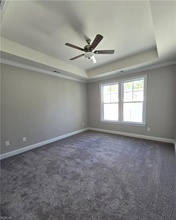 empty room featuring ceiling fan, dark carpet, a raised ceiling, and ornamental molding