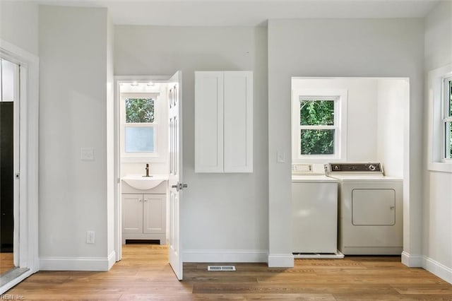 laundry area with light wood-type flooring, sink, plenty of natural light, and independent washer and dryer