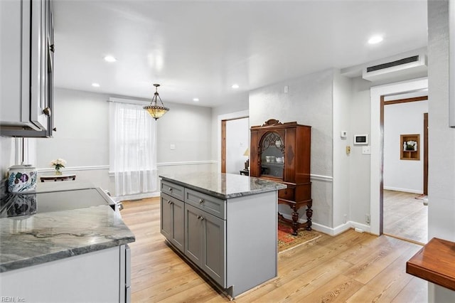 kitchen with gray cabinetry, stone counters, a center island, pendant lighting, and light hardwood / wood-style flooring