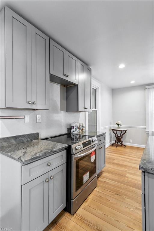 kitchen with gray cabinetry, electric stove, light hardwood / wood-style flooring, and dark stone counters