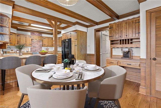 dining space with beamed ceiling, light hardwood / wood-style floors, crown molding, and sink