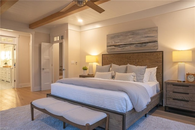 bedroom with light hardwood / wood-style floors, beamed ceiling, connected bathroom, and ceiling fan