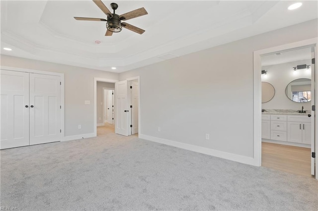 unfurnished bedroom with connected bathroom, a raised ceiling, light colored carpet, and ceiling fan