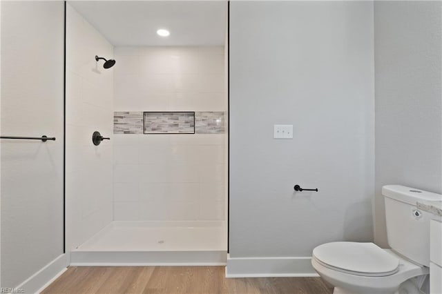 bathroom with toilet, hardwood / wood-style flooring, and tiled shower