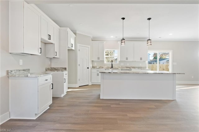 kitchen with hanging light fixtures, white cabinetry, light wood-type flooring, a center island, and sink