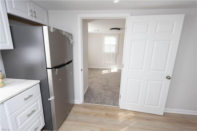 kitchen with stainless steel fridge, white cabinets, and light wood-type flooring