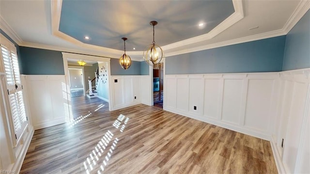 unfurnished dining area featuring crown molding, wood-type flooring, and a raised ceiling