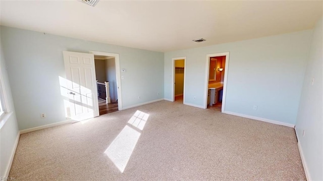 unfurnished bedroom featuring connected bathroom, light carpet, a closet, and a walk in closet