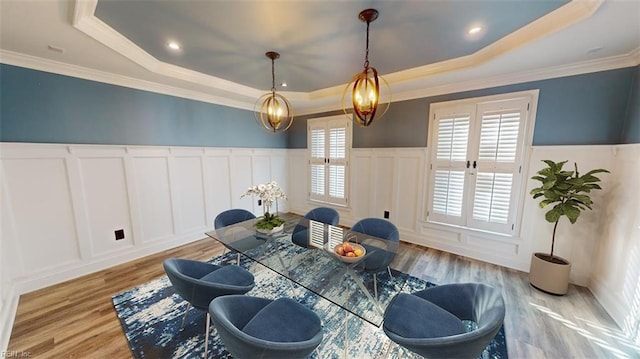 dining space with crown molding, light wood-type flooring, and a raised ceiling