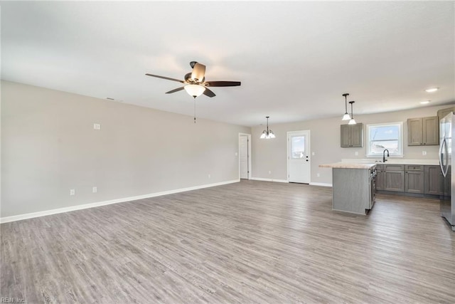 unfurnished living room featuring light wood finished floors, a ceiling fan, baseboards, and a sink