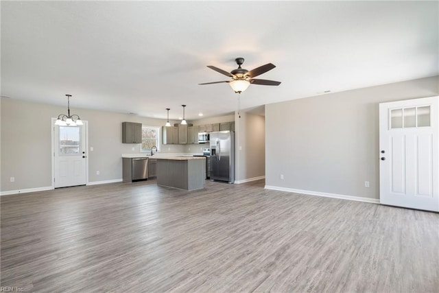 unfurnished living room featuring hardwood / wood-style flooring, sink, and ceiling fan with notable chandelier