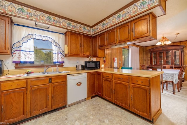 kitchen featuring crown molding, a notable chandelier, white dishwasher, sink, and kitchen peninsula