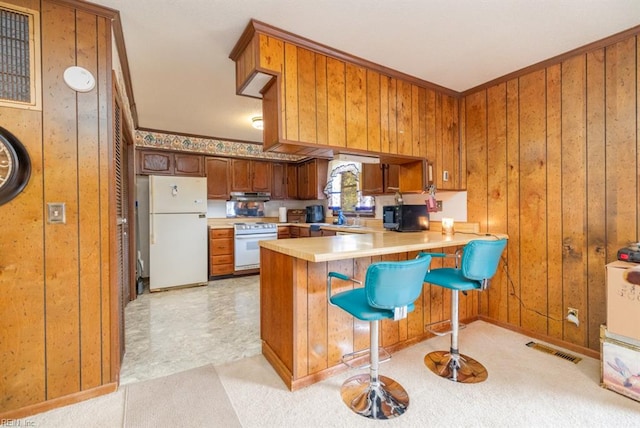 kitchen with wood walls, white appliances, a breakfast bar, and kitchen peninsula