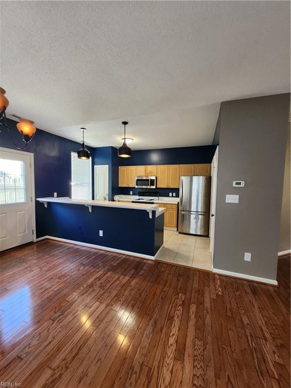 kitchen featuring appliances with stainless steel finishes, a textured ceiling, a kitchen breakfast bar, hanging light fixtures, and light hardwood / wood-style floors