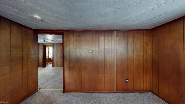 unfurnished room with wooden walls, light colored carpet, and a textured ceiling