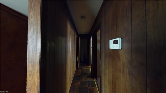 hallway featuring dark tile patterned floors, lofted ceiling, and wooden walls