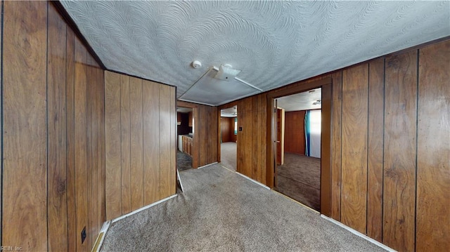 empty room with carpet, wood walls, and a textured ceiling