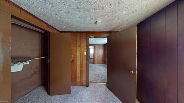 hallway featuring light colored carpet and wooden walls