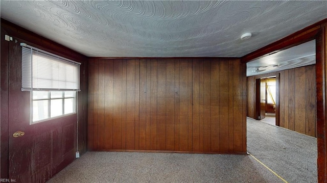 carpeted empty room with a textured ceiling and wood walls