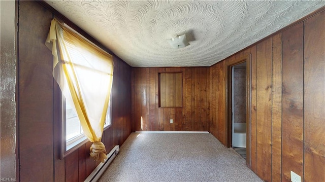 carpeted empty room with a baseboard radiator, wooden walls, and a textured ceiling