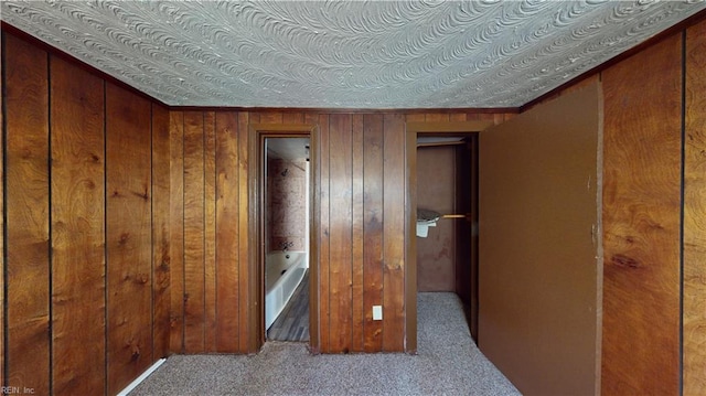 unfurnished bedroom featuring light colored carpet, a textured ceiling, and wooden walls