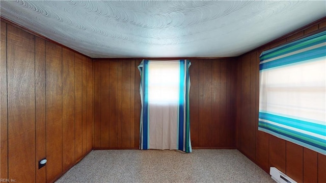 carpeted empty room featuring wooden walls, a baseboard radiator, and a wealth of natural light